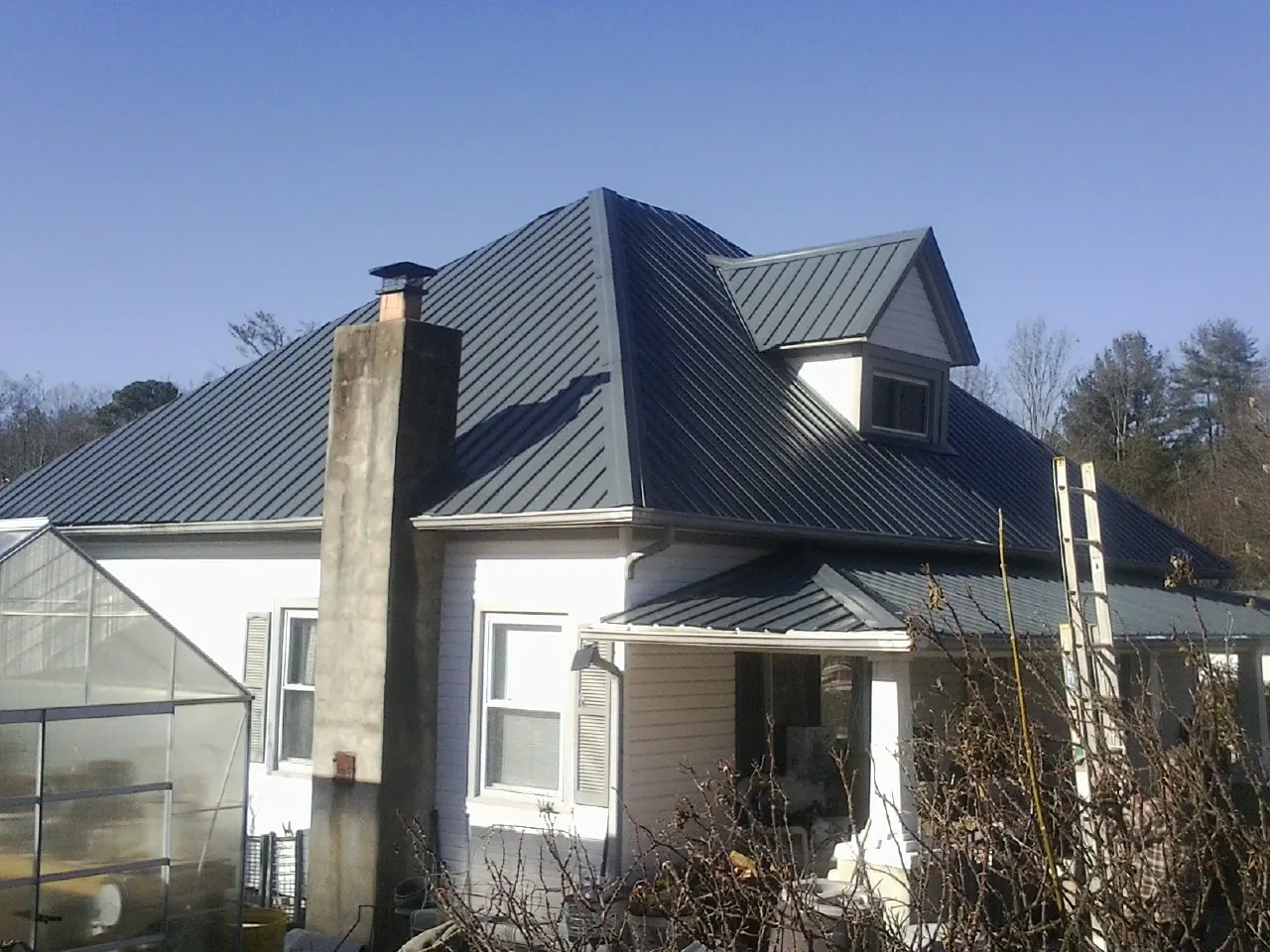Dark blue standing seam metal roof on a white farmhouse with dormer — Slate & Tile Roof Repair by Roofing Brothers in Roans Prairie