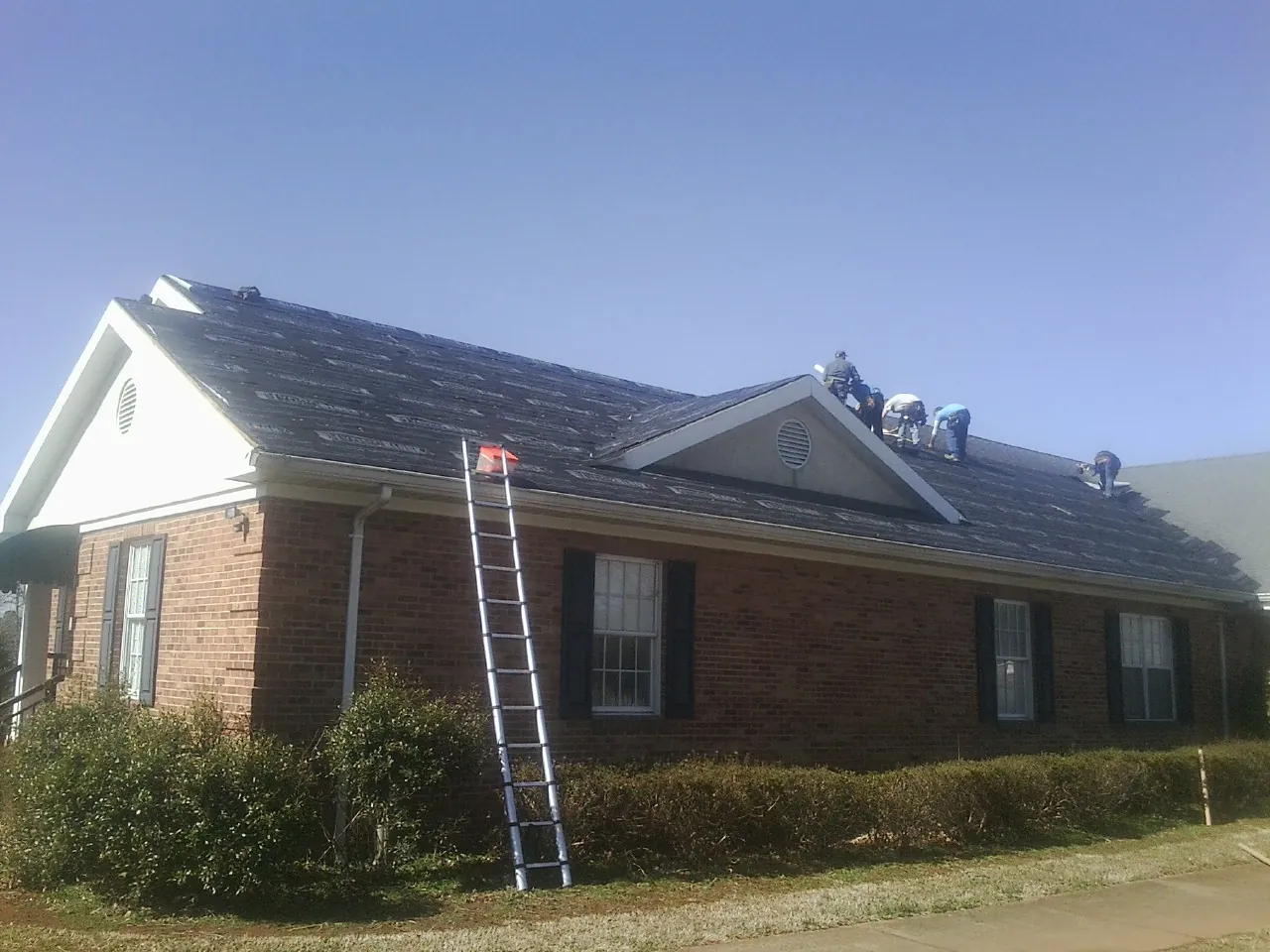 Crew tearing shingles off a brick ranch roof with a ladder set — Emergency Roof Repair work by our crew in Roans Prairie