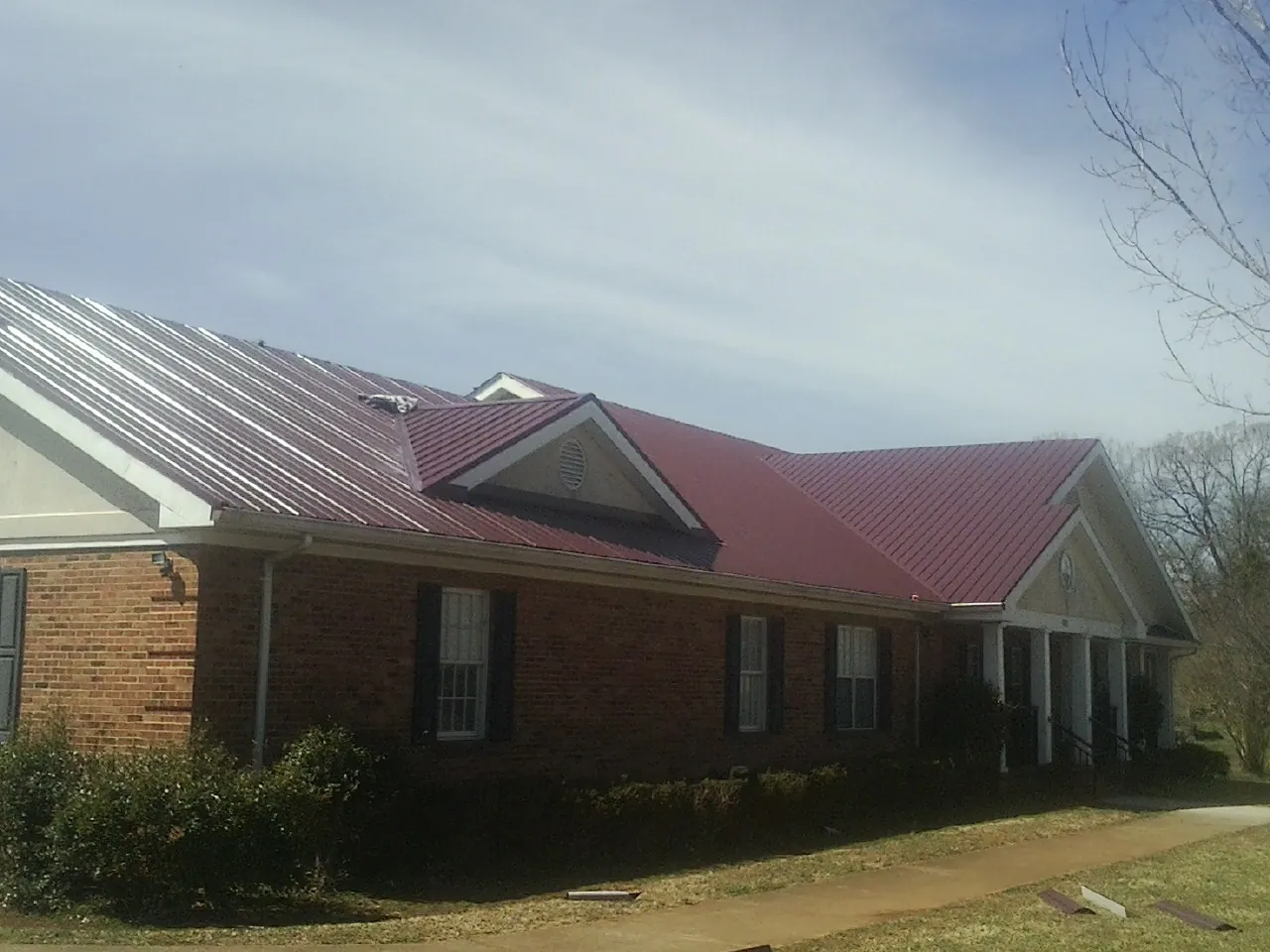 Red metal roof with gabled entries on a long brick building, from a Hail Damage Roof Repair job in Roans Prairie