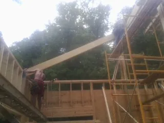Carpenter raising a rafter beam on a new second story frame in Roans Prairie