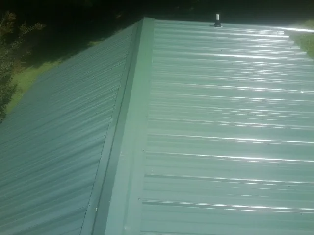 New green metal panels meeting at the ridge of a roof — Flat Roof Repair work by our crew in Roans Prairie