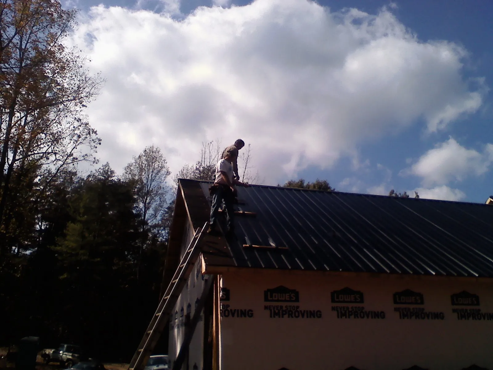 Roofer fastening dark metal panels high against a cloudy sky, from a Roof Inspection job in Roans Prairie