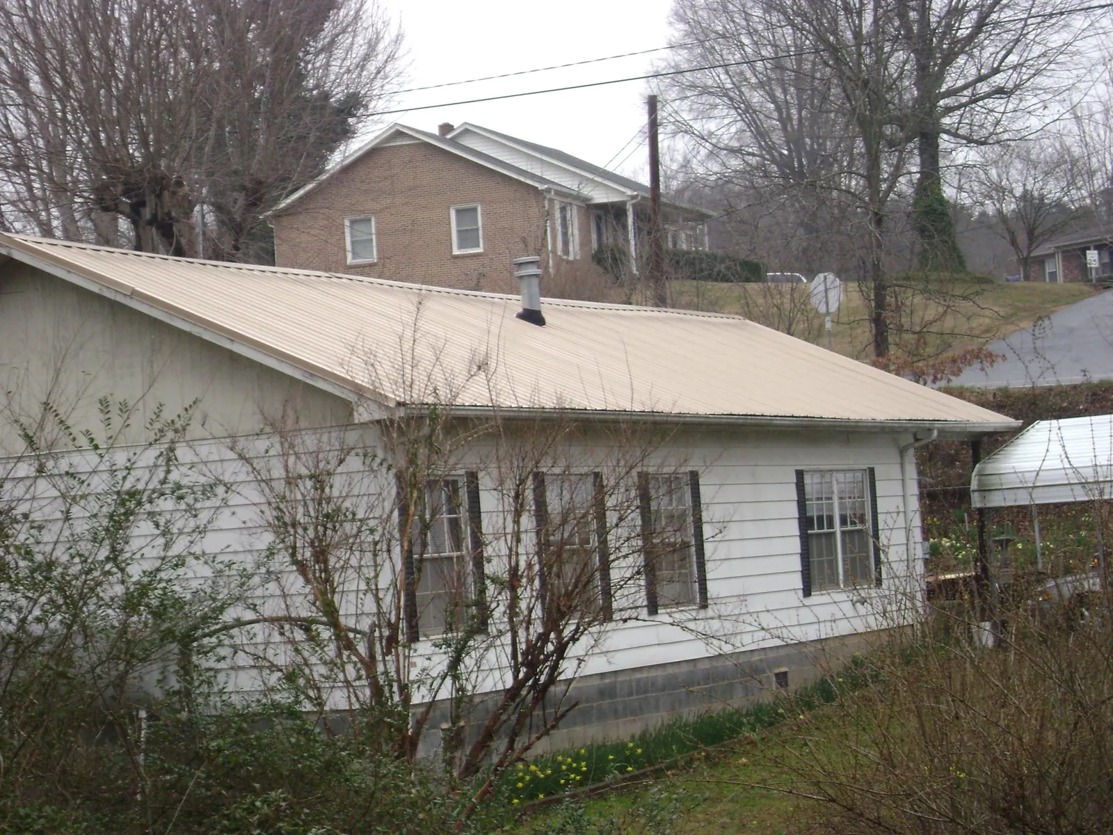 Tan metal roof on a white sided house set into a hillside — Commercial Roofing by Roofing Brothers in Roans Prairie