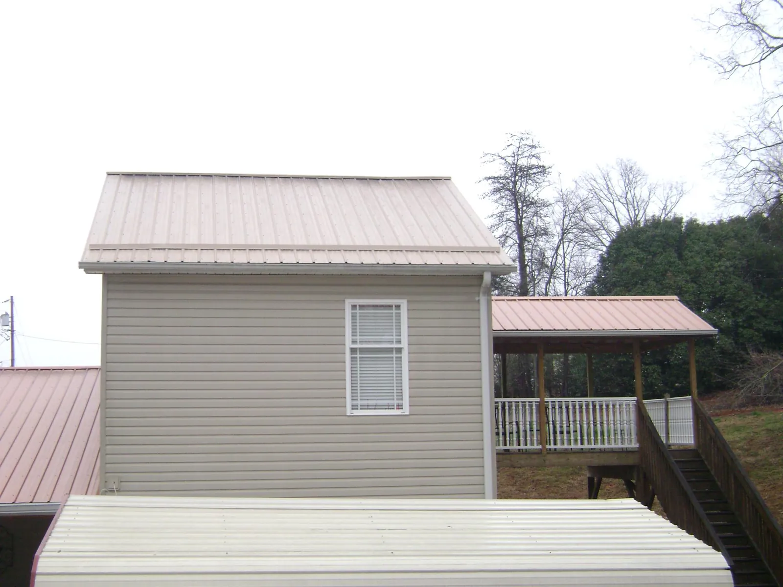 Tan metal roofs on a two story addition and attached porch, from a Roof Replacement job in Roans Prairie